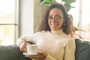 donna latina che beve caffè sul divano di casa foto