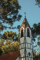 nova petropolis, brasile - 20 luglio 2019. campanile dalla chiesa in stile tradizionale con influenze tedesche tra diversi alberi nel parco del villaggio di immigrati di nova petropolis. foto