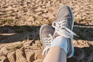 gambe in scarpe da ginnastica grigie sulla sabbia della spiaggia. foto