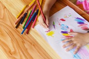 ragazza che dipinge su un foglio di carta con matite colorate sul tavolo di legno a casa - bambino che fa un disegno e pastello colorato foto