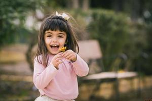 bambina che cattura un fiore in un parco. sorridente e felice con un fiore. copia spazio foto