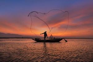 pescatore asiatico con la sua barca di legno nel fiume naturale al mattino presto prima dell'alba foto