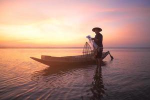 pescatore asiatico con la sua barca di legno che tiene una rete pronta per catturare pesci d'acqua dolce nel fiume naturale all'inizio durante l'ora dell'alba foto