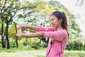 la giovane donna asiatica riscalda il corpo che si estende prima dell'esercizio mattutino e dello yoga nel parco sotto la calda luce del mattino. giovane donna asiatica in buona salute che si esercita al parco. concetto all'aperto di esercizio della donna. foto