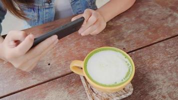 blogger femminile che fotografa la tazza di tè verde nella caffetteria con il suo telefono. una giovane donna che cattura foto di tè caffè su smartphone, fotografando il pasto con la fotocamera mobile.