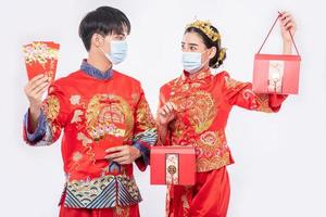 uomo e donna indossano maschera e cheongsam con in mano denaro regalo rosso e borsa rossa foto