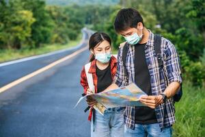 turisti maschi e femmine indossano maschere mediche e guardano la mappa per strada. foto