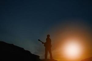 ombra di un uomo in piedi e suonare la chitarra su un'alta collina. foto