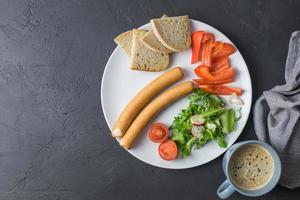 salsicce cotte con lattuga, paprika di pomodoro e pane su un piatto bianco vista dall'alto spazio per il testo foto