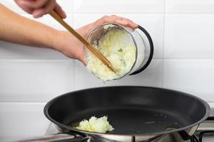 una persona che getta le cipolle tritate nella padella. preparazione del pasto. foto