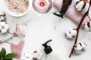 rullo di giada massaggio viso con prodotto cosmetico su sfondo di marmo bianco