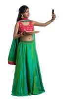 bella giovane ragazza felice che prende un selfie con lampada di argilla o diya durante il festival della luce diwali utilizzando uno smartphone su sfondo bianco foto
