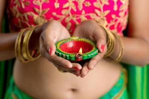 ritratto di una ragazza tradizionale indiana che tiene diya, ragazza che celebra diwali o deepavali con in mano una lampada a olio durante il festival della luce su sfondo bianco foto