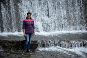 una bella giovane donna che posa sulla riva del fiume e si diverte o gioca con l'acqua in eccesso dal fiume. foto