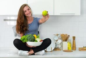 foto candida di giovane donna sportiva caucasica seduta su coutner in cucina e mangiando una sana colazione biologica. concetto di cura di sé