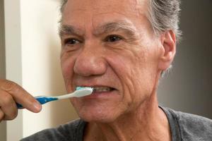 uomo maturo che si lava i denti con uno spazzolino da denti consumato foto