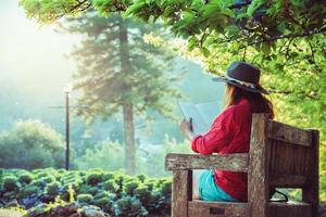 natura di viaggio donna asiatica. viaggiare rilassati. leggi il libro sulla panchina del parco in estate. foto