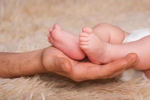 papà tiene tra le mani un bambino piccolo. piccole gambe di un neonato in grandi mani di papà. massaggio ai piedi del bambino