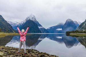 giovane viaggiatore asiatico che celebra il successo a Milford Sound, Parco Nazionale di Fiordland, Isola del Sud, Nuova Zelanda foto