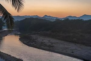 tramonto sulle montagne con fiume e palma foto