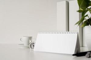 simulare un calendario a spirale vuoto con fogli ribaltabili su un tavolo bianco con caffè, cancelleria e orologio foto