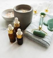 rullo di giada massaggio viso con prodotto cosmetico su sfondo di marmo bianco foto