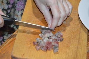 affettare le aringhe con un coltello su un tagliere da cucina foto