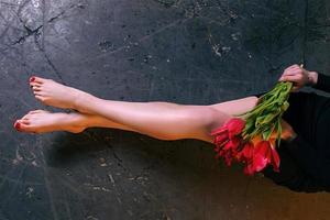 modello di belle gambe di donna lisce e snelle dopo la depilazione laser sullo sfondo di cemento grezzo con fiori di tulipani foto
