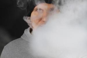 molto fumo bianco - il vaper esala una nuvola di fumo su sfondo scuro, l'uomo vape messa a fuoco selettiva foto