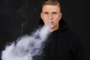 molto fumo bianco - il vaper esala una nuvola di fumo su sfondo scuro, l'uomo vape messa a fuoco selettiva foto