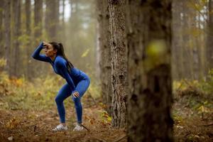 la giovane donna si prende una pausa durante l'esercizio all'aperto sul sentiero nel bosco in autunno foto