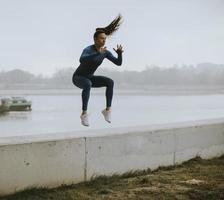 giovane donna in tuta blu che fa un salto in riva al fiume al mattino d'autunno foto
