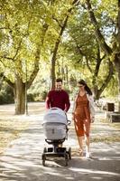 giovani genitori felici che camminano nel parco e guidano un bambino in carrozzina foto