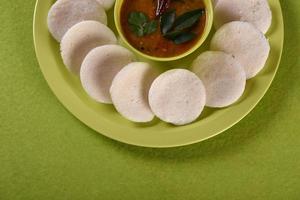 idli con sambar in una ciotola su sfondo verde, piatto indiano cibo preferito dell'India meridionale rava idli o semolino pigramente o rava pigramente, servito con sambar e chutney di cocco verde. foto