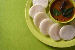 idli con sambar in una ciotola su sfondo verde, piatto indiano cibo preferito dell'India meridionale rava idli o semolino pigramente o rava pigramente, servito con sambar e chutney di cocco verde. foto