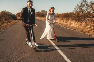 sposi sorridenti in sella a uno scooter lungo la strada fuori città al tramonto. posto per testo o pubblicità foto