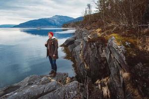 giovane con uno zaino giallo che indossa un cappello rosso in piedi su una roccia sullo sfondo della montagna e del lago. spazio per il tuo messaggio di testo o contenuto promozionale. concetto di stile di vita di viaggio foto