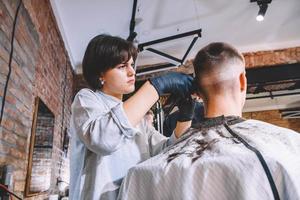 bella donna parrucchiere fa un taglio di capelli la testa del cliente con un trimmer elettrico nel negozio di barbiere. pubblicità e concetto di negozio di barbiere. posto per testo o pubblicità foto