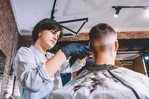 bella donna parrucchiere fa un taglio di capelli la testa del cliente con un trimmer elettrico nel negozio di barbiere. pubblicità e concetto di negozio di barbiere. posto per testo o pubblicità