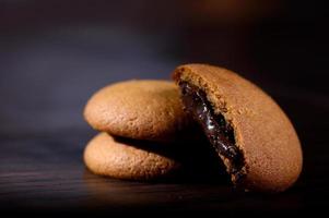 biscotti ripieni di crema al cioccolato. biscotti alla crema di cioccolato. biscotti al cioccolato marrone con ripieno di crema su sfondo nero. foto