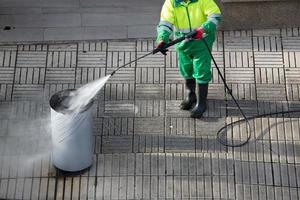 spazzatrice che pulisce un bidone della spazzatura sul marciapiede con una macchina a getto d'acqua ad alta pressione. manutenzione delle strade foto