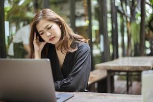 donna asiatica stressata che sente mal di testa nel negozio di caffè foto