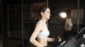 la bella donna asiatica di sport sta correndo sul tapis roulant in palestra foto