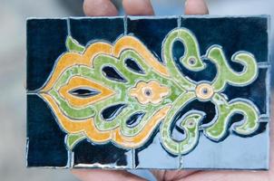 asiatico vecchio mosaico in ceramica. elementi di ornamento orientale su piastrelle di ceramica. uomo che tiene un campione foto