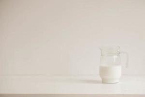 brocca di vetro con latte su un tavolo bianco foto
