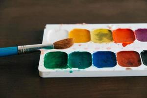 set di colori ad acquerello con un pennello per dipingere su uno sfondo di legno scuro foto
