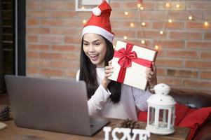 giovane donna sorridente che indossa un cappello rosso di babbo natale che fa videochiamata sul social network con la famiglia e gli amici il giorno di natale. foto