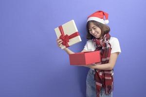 Ritratto di bella donna che indossa il cappello rosso di Babbo Natale che tiene una confezione regalo su sfondo per studio, concetto di Natale e Capodanno