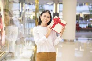 donna che tiene una confezione regalo nel centro commerciale, il ringraziamento e il concetto di natale.