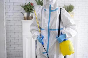 uno staff medico in tuta dpi sta usando spray disinfettante in soggiorno, protezione covid-19, concetto di disinfezione.